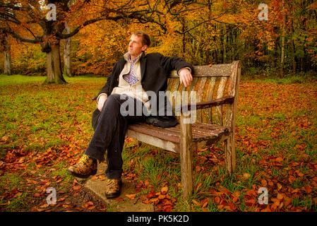 Ein Mann im Winter Kleidung sitzt und entspannt auf einer Parkbank Stockfoto