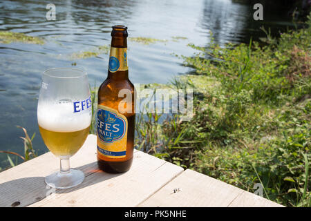 Kalte Flasche EFES Pilsener Malz Bier auf einer hölzernen Steg auf dem Fluss Azmac, Akyaka, Provinz Mugla, Türkei Stockfoto