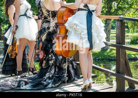 Musik und Natur Konzept. Weibliche musikalischen Quartetts mit Saiteninstrumenten, ein Cello und drei Violinen, stehend auf Brücke, bereitet sich in der Natur zu spielen Stockfoto