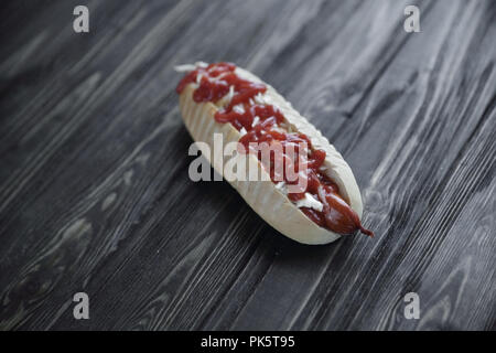 Hot Dog mit pikanter Sauce auf dunklem Hintergrund. Foto mit Kopie Raum Stockfoto