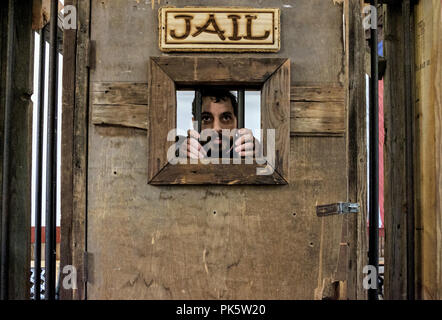 Mann mit Schnurrbart hält die Bars in einem Gefängnis Fenster, wie er aus seiner alten hölzernen Zelle in Dallas - Fort Worth Stock Yards aussieht. Horizontale. Stockfoto