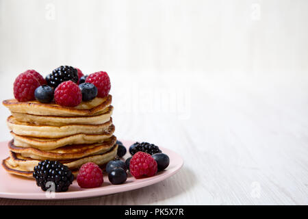 Pfannkuchen mit Beeren auf einem Rosa die Platte über der weißen Holz- Hintergrund, Seitenansicht. Kopieren Sie Platz. Stockfoto