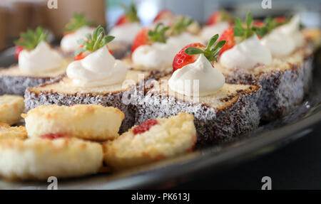 Tea Party. Bis Nahaufnahmen von Schokolade lamington Kuchen mit einem klacks Sahne und Garnieren von Erdbeere auf der Oberseite. Ein Tablett mit süssen Tee am Morgen b Stockfoto