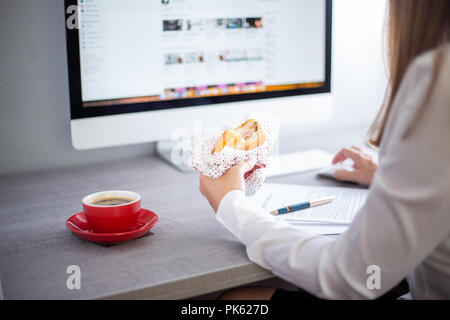 Young Business Frau Burger essen am Schreibtisch Stockfoto