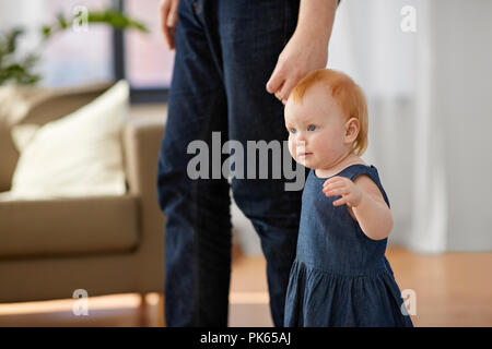 Baby Mädchen gehen mit Vaters Hilfe zu Hause Stockfoto