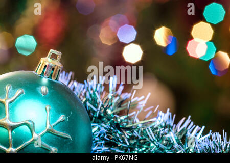 Eine große Glaskugel mit einem Muster von Schneeflocken. Im Hintergrund verschwommen Lichter von einem Weihnachtsbaum. Boke. Weihnachten Spielzeug in der Weihnachtszeit Lametta. Stockfoto