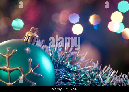 Eine große Glaskugel mit einem Muster von Schneeflocken. Im Hintergrund verschwommen Lichter von einem Weihnachtsbaum. Boke. Weihnachten Spielzeug in der Weihnachtszeit Lametta. Stockfoto