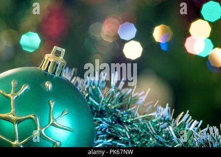 Eine große Glaskugel mit einem Muster von Schneeflocken. Im Hintergrund verschwommen Lichter von einem Weihnachtsbaum. Boke. Weihnachten Spielzeug in der Weihnachtszeit Lametta. Stockfoto