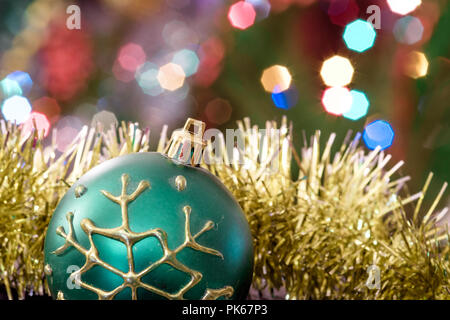 Eine große Glaskugel mit einem Muster von Schneeflocken. Im Hintergrund verschwommen Lichter von einem Weihnachtsbaum. Boke. Weihnachten Spielzeug in der Weihnachtszeit Lametta. Stockfoto