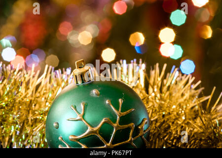Eine große Glaskugel mit einem Muster von Schneeflocken. Im Hintergrund verschwommen Lichter von einem Weihnachtsbaum. Boke. Weihnachten Spielzeug in der Weihnachtszeit Lametta. Stockfoto