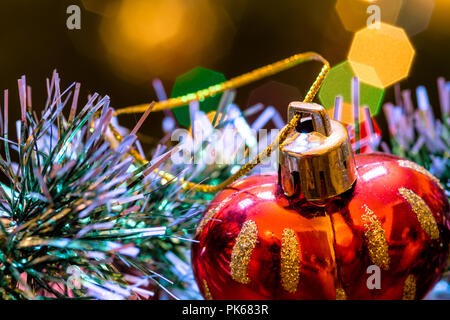Eine große Glaskugel mit einem Muster von Schneeflocken. Im Hintergrund verschwommen Lichter von einem Weihnachtsbaum. Boke. Weihnachten Spielzeug in der Weihnachtszeit Lametta. Stockfoto