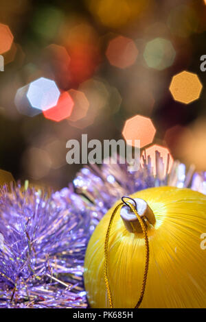 Eine große Glaskugel mit einem Muster von Schneeflocken. Im Hintergrund verschwommen Lichter von einem Weihnachtsbaum. Boke. Weihnachten Spielzeug in der Weihnachtszeit Lametta. Stockfoto
