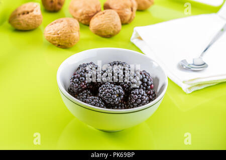 Köstliche frische Brombeeren und reif, schwarz und rötlich Granat. In weiße Schüssel an der grünen und weißen Hintergrund. Mit Walnüssen. Stockfoto
