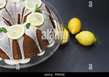 Ganze Zitrone Frischkäse bundt Cake mit Scheiben von frischen Zitronen und Minze. Extrem flache Tiefenschärfe mit selektiven Fokus auf Kuchen. Stockfoto