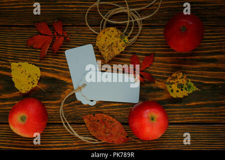 Mock up, weiße Etiketten, Folien, Papier mit roten Äpfeln mit gelben und roten Blätter im Herbst auf Holz gebürstet Hintergrund Stockfoto