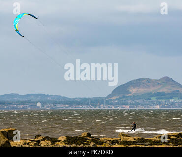 Longniddry Bents, East Lothian, Schottland, UK, 11. September 2018. UK Wetter: 40 MPH Winde an einem sonnigen Tag schaffen gute Voraussetzungen für die bunten Kite Surfer der Firth-of-Forth, mit der charakteristischen Umrisse von Arthur's Seat und die Edinburgh City Skyline über die Bucht Stockfoto