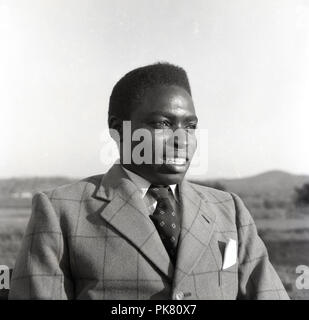 1950, historische, ein Portrait eines gut gekleideten jungen ugandischen Mann mit einem Check gemusterte Jacke und Krawatte und mit einem handerchief in der Vordertasche. Stockfoto