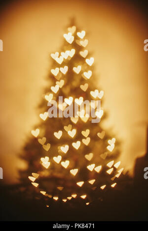 Schönen Weihnachtsbaum Golden Lights Herzen im festlichen Raum. Weihnachten Abstract Background, Blur defokussierten Bokeh der gelb leuchtenden Herzen auf christm Stockfoto