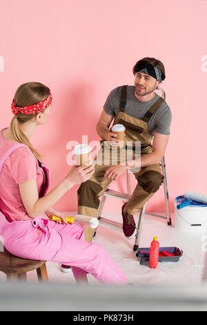 Frau auf Stuhl mit Papier Tasse Kaffee und Freund sitzen auf Leiter mit Tasse Kaffee in dem Zimmer mit den Malwerkzeugen Stockfoto