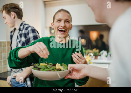 Junge Frau lachend mit ihren Freunden bei einem Abendessen, als sie Zitronensaft auf einen Salat presst. Stockfoto
