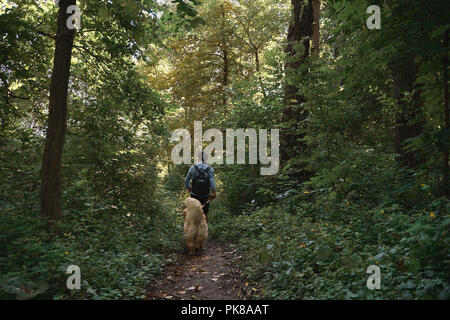 Schöner Mann seinen Hund im Wald einen Weg. Happy golden retriever Spaziergänge in der Nähe von seinen männlichen besten Freund Stockfoto