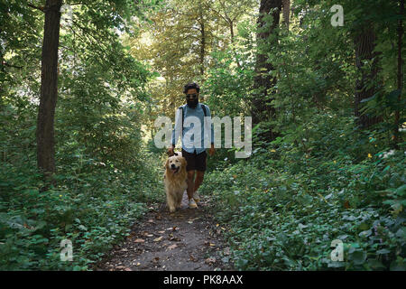 Schöner Mann seinen Hund im Wald einen Weg. Happy golden retriever Spaziergänge in der Nähe von seinen männlichen besten Freund Stockfoto