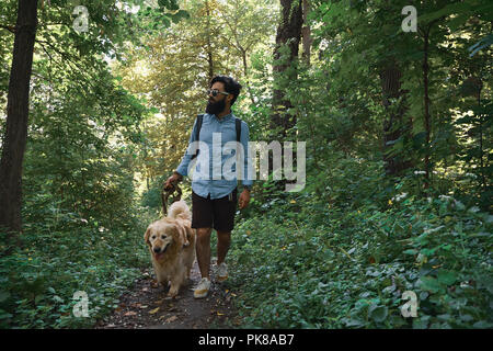 Schöner Mann seinen Hund im Wald einen Weg. Happy golden retriever Spaziergänge in der Nähe von seinen männlichen besten Freund Stockfoto