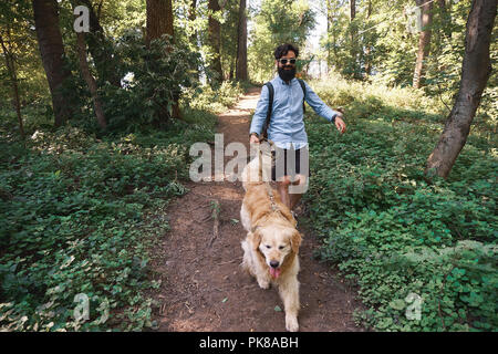 Schöner Mann seinen Hund im Wald einen Weg. Happy golden retriever Spaziergänge in der Nähe von seinen männlichen besten Freund Stockfoto