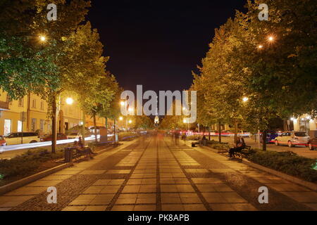 Night Skyline der Stadt Tschenstochau, Polen, wichtigster Vertreter avenue tith Bäume auf beiden Seiten, der Turm der Kathedrale am Horizont, Langzeitbelichtung. Stockfoto