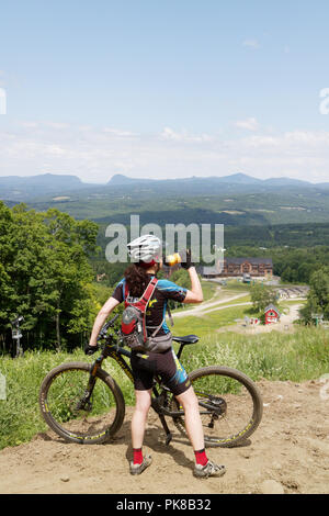 Eine Dame Mountainbiker (in ihrem 40s) Pausen Wasser auf das Königreich Trails mountain bike Park im Osten Burke, Vermont, USA zu trinken Stockfoto