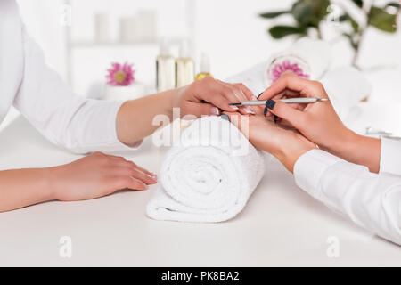 7/8 Schoß der Frau, Maniküre, Kosmetikerin mit cuticle Pusher am Tisch mit Blumen und Handtücher im Beauty Salon Stockfoto