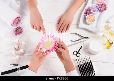 Blick von oben auf die Frau zeigt auf Proben des Nagellacke in die Hände der Maniküre am Tisch mit Nagellacke, Nagelfeilen, Nagelscheren, nagelhaut Pusher, Stockfoto