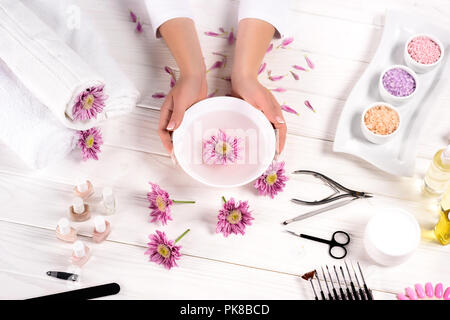 Teilweise Bild der Frau mit Badewanne für Nägel über Tisch mit Blumen, Handtücher, bunt Meersalz, Aroma öl Flaschen, Nagellacke, creme Container einen Stockfoto
