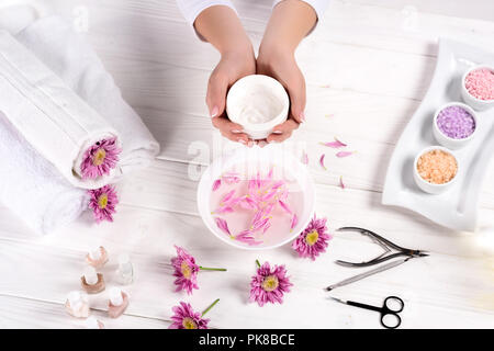 7/8 Schuß von Frau mit Sahne über Tabelle mit Badewanne für Nägel, Blumen, Handtücher, bunt Meersalz, Nagellacke und Tools für Maniküre in Schönheit Stockfoto