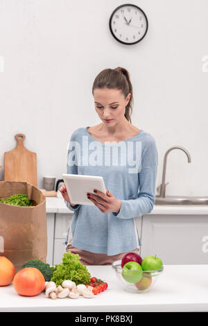 Attraktive Frau mit Tablet Prüfung Liste der kauft nach Einkaufen zu Hause Stockfoto