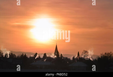 Herrliche Winterlandschaft mit einem taub Dorf, Rauchende Schlote und Kirchturm, einer farbenfrohen Sonnenaufgang, auf einem Dezember Morgen, in Deutschland. Stockfoto