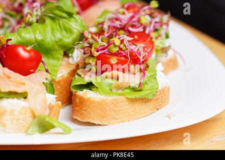 Hausgemachte kleine Sandwiches mit Sprossen, weißer Käse Salat, coctail Tomaten und Räucherlachs auf weiße Platte Stockfoto