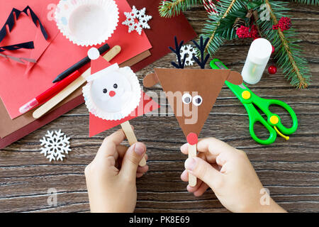 Ein Kind hält Weihnachten Weihnachtsmann und Rentier stics Puppen. Handgefertigt. Projekt der Kreativität der Kinder, Kunsthandwerk, Handwerk für Kinder. Stockfoto