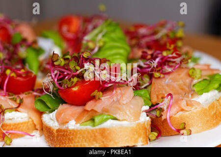 Hausgemachte kleine Sandwiches mit Sprossen, weißer Käse Salat, coctail Tomaten und Räucherlachs auf weiße Platte Stockfoto