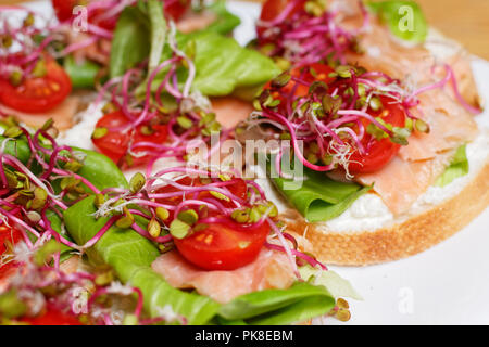 Hausgemachte kleine Sandwiches mit Sprossen, weißer Käse Salat, coctail Tomaten und Räucherlachs auf weiße Platte Stockfoto