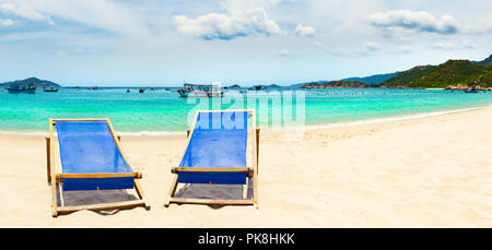 Schönen weißen Sandstrand. Stühle im Vordergrund, Fischerboote auf Hintergrund. Landschaft von Vietnam. Panorama Stockfoto