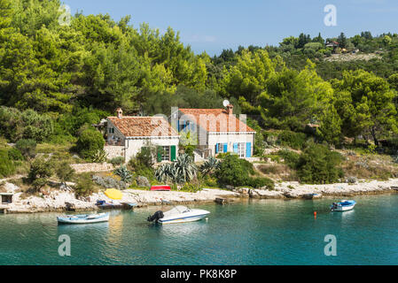 Naturstein Häuser mit terrakottafarbenen Fliesen Dach, Boote und Kiefernwald an der felsigen Küste mit türkisblauem Meer auf der Insel Losinj, Kroatien Stockfoto