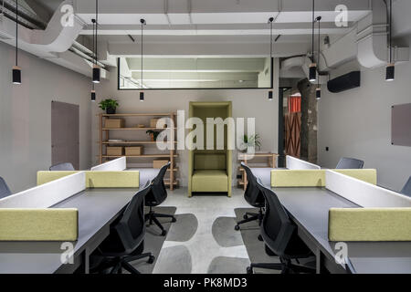 Stilvolle Büro im Loft Stil mit hellen Wänden. Es gibt graue Tabellen mit Trennwänden, schwarze Stühle, Regale mit Kästen und Pflanzen, grüne Fancy Stockfoto