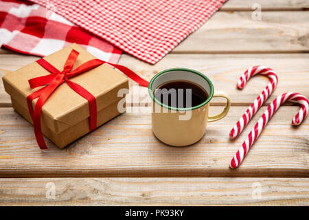 Der Weihnachtszeit. Tasse Kaffee mit Zuckerstangen und eine Geschenkverpackung mit roter Schleife auf hölzernen Hintergrund Stockfoto