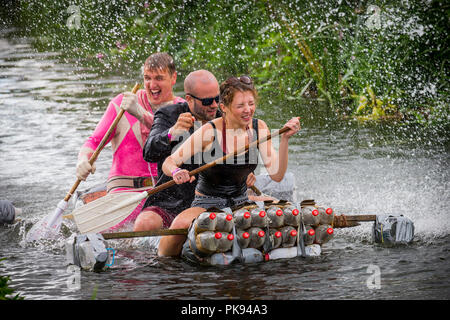 Drei Leute auf einem Floß von Cola Flaschen werden mit Wasser aus einem Schlauch während paddeln entlang eines Flusses im Tiefland Spiele gespritzt Stockfoto
