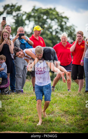 Mann, der eine Frau über eine schmutzige und nasse Hindernisparcours im Tiefland Spiele in Thorney, Somerset, England Stockfoto