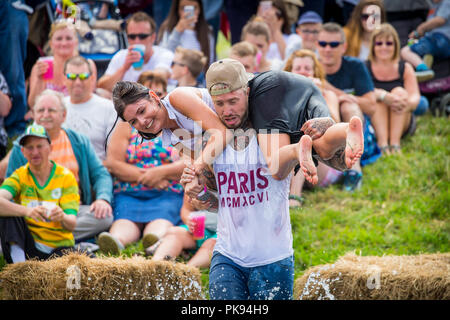 Mann, der eine Frau über eine schmutzige und nasse Hindernisparcours im Tiefland Spiele in Thorney, Somerset, England Stockfoto