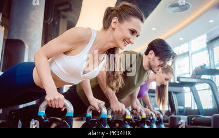 Drei junge Leute, die KETTLEBELL plank Herausforderung Stockfoto