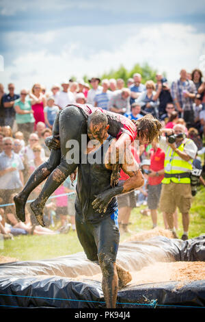 Mann, der eine Frau über eine schmutzige und nasse Hindernisparcours im Tiefland Spiele in Thorney, Somerset, England Stockfoto