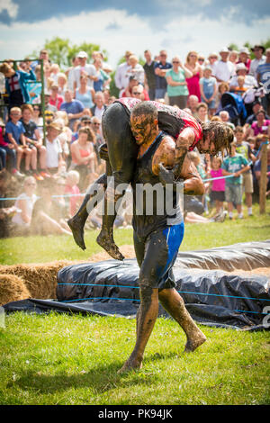 Mann, der eine Frau über eine schmutzige und nasse Hindernisparcours im Tiefland Spiele in Thorney, Somerset, England Stockfoto